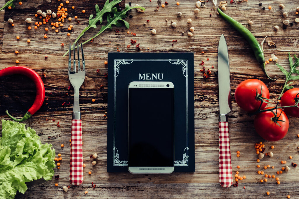 Menu digitale su tablet con posate, verdure fresche e spezie su tavola in legno rustico