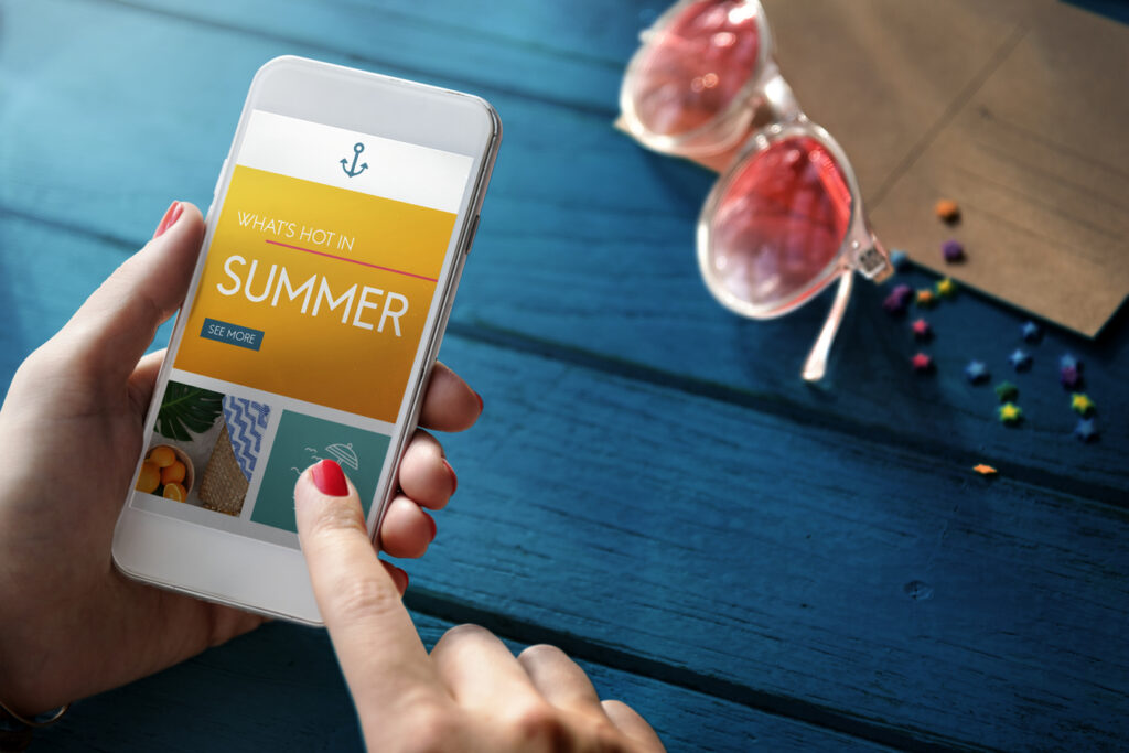 Smartphone che mostra app con offerte estive, bicchieri da cocktail sul tavolo in legno